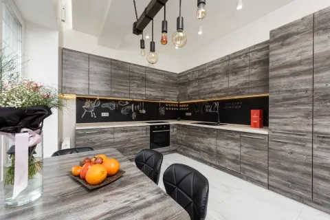 Table with bouquet and fruits placed near gray cupboards and modern kitchenware in spacious kitchen with lamps and creative design